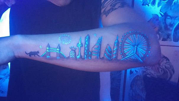 Arm with glow in the dark tattoo of a city skyline, visible under black light.
