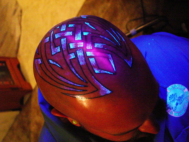 Glow in the dark tattoo design on a shaved head, illuminated under black light.