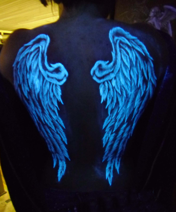 Glow in the dark tattoos of angel wings visible under black light on a person's back.