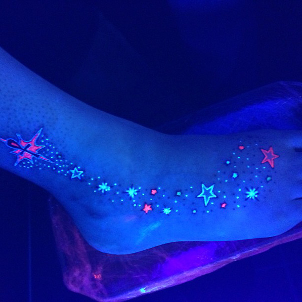 Glowing stars and patterns on a foot tattoo under black light.