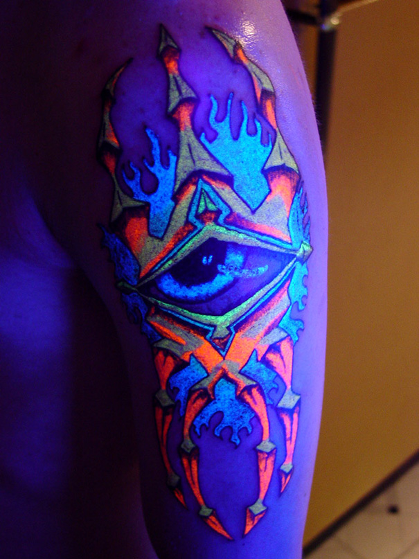 Glow in the dark tattoo of a colorful eye design, visible under black light on arm.