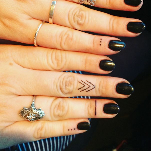 Minimalist tattoos on fingers with black nail polish and silver rings.