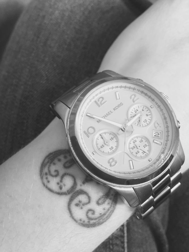 Minimalist tattoo of spirals on a wrist underneath a wristwatch.