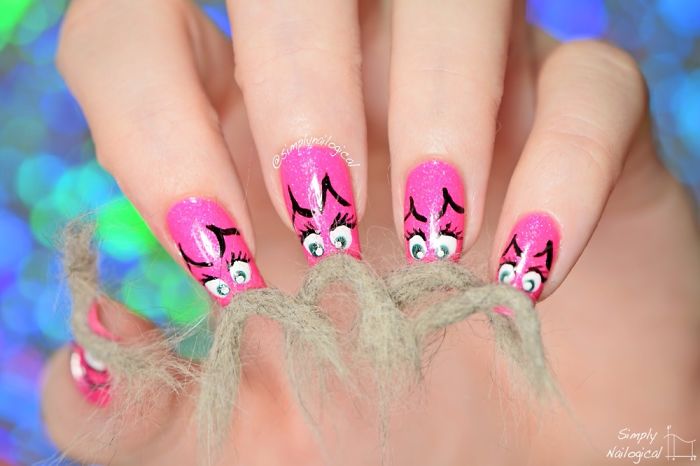 Close-up of pink furry nails with cartoon eyes and black designs on a blurred blue background.
