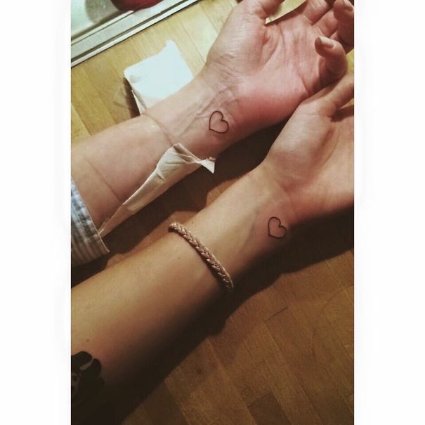 Two wrists with matching heart tattoos, symbolizing sisterly bond.
