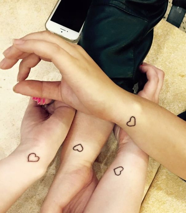 Four wrists with matching heart tattoos, each symbolizing the bond between sisters.