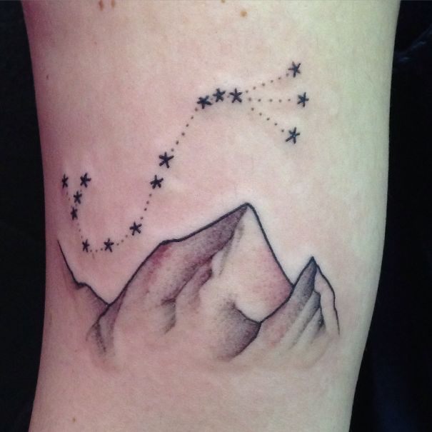 Minimalist tattoo of mountains and constellation on forearm, featuring simple black ink design.