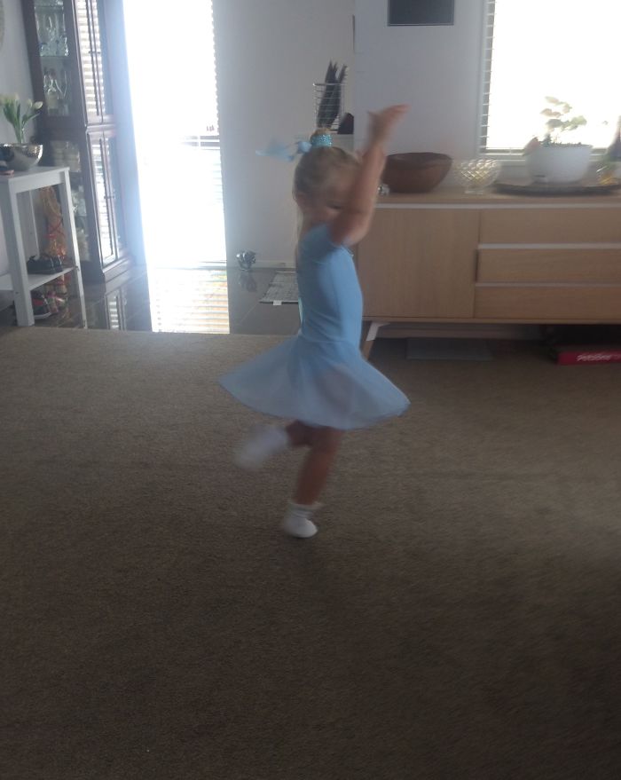 Young girl in a blue ballet dress twirling in a living room, celebrating Ballet Day.