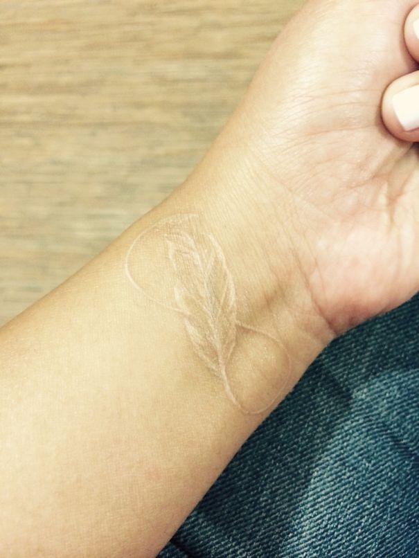 Minimalist wrist tattoo depicting a delicate white ink feather on skin.