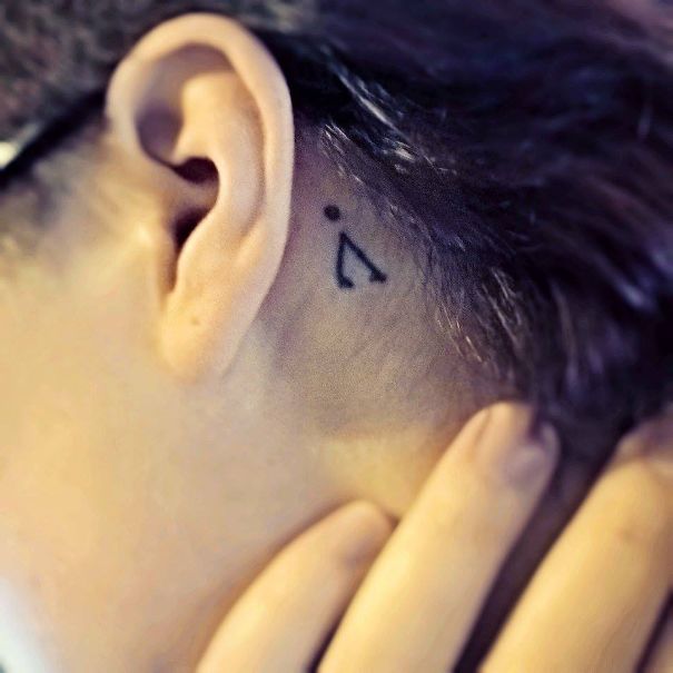 Minimalist tattoo of a small geometric shape behind the ear.