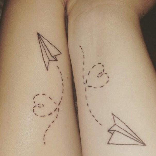Minimalist paper plane sister tattoos symbolizing connection and bond on arms.