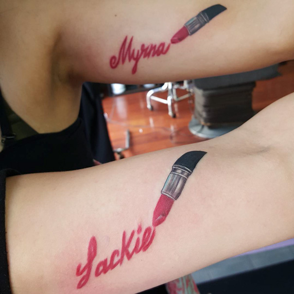 Two arms with matching lipstick sister tattoos in red cursive font.