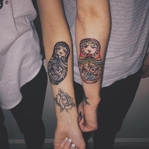 Matching sister tattoos featuring colorful and black-and-white matryoshka dolls on forearms, symbolizing sisterly bond.