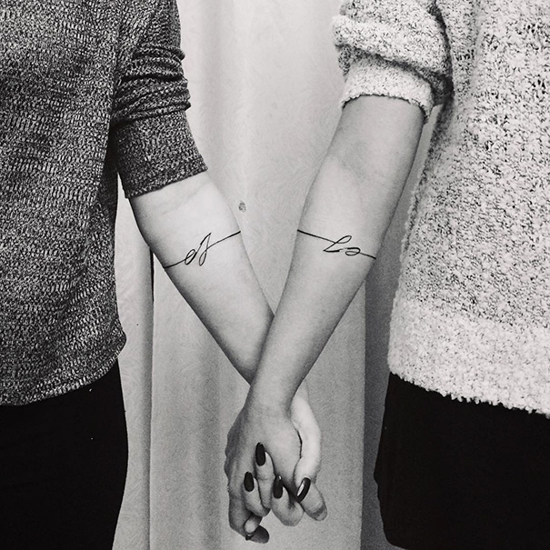 Sisters holding hands, showcasing minimalistic tattoos on forearms symbolizing their bond.
