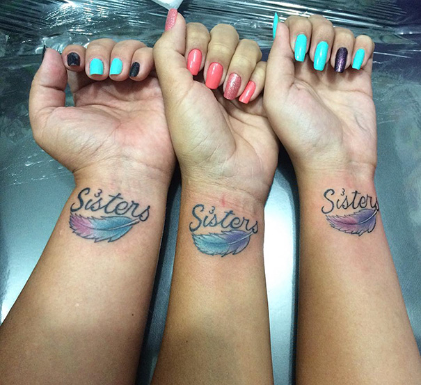 Three wrists with matching "Sisters" tattoos featuring colorful feathers.