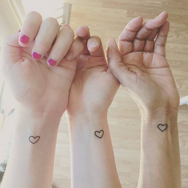 Three wrists with matching heart tattoos symbolizing sister bond.