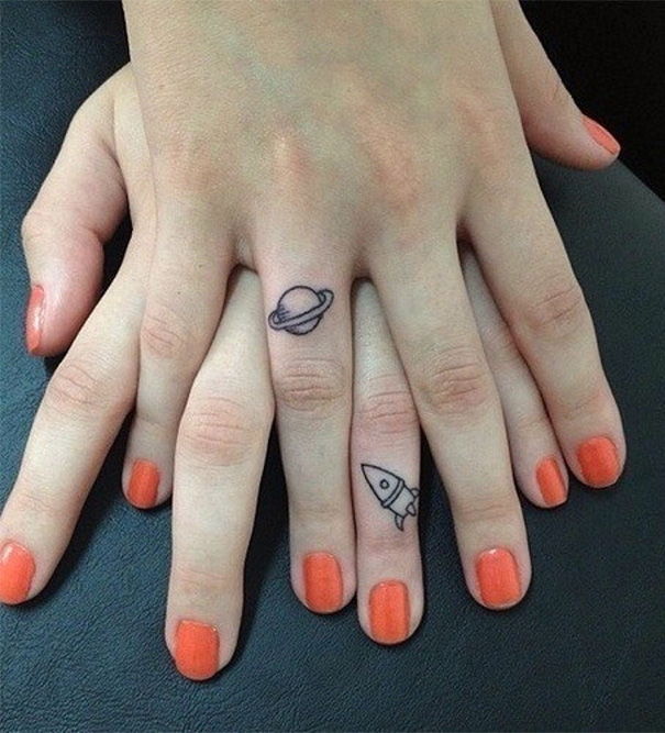 Close-up of hands with sister tattoos on fingers, featuring a planet and a rocket design.