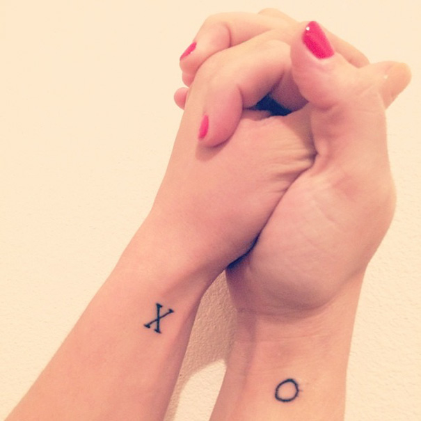 Two wrists with sister tattoos, XO design, clasped together to symbolize a strong bond.