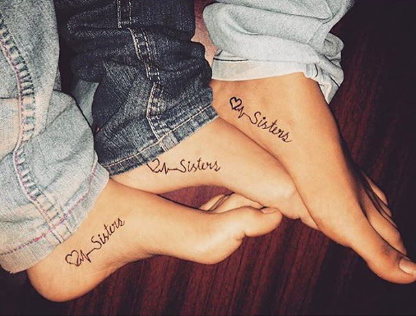 Three feet with matching sister tattoos featuring hearts and the word "sisters".