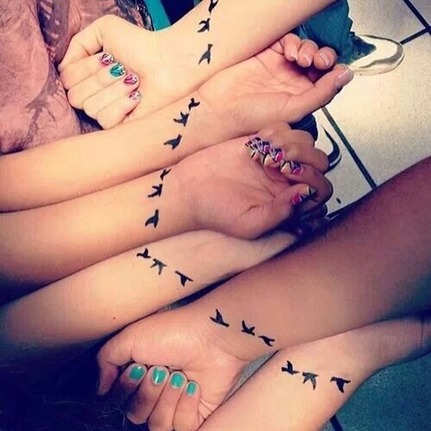 Arms with matching bird tattoo designs symbolizing sister bond.