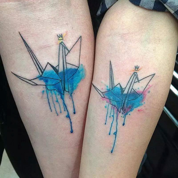 Matching watercolor origami crane sister tattoos symbolizing sibling bond.