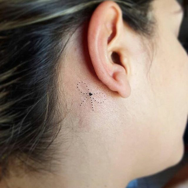 Minimalist tattoo of a small dragonfly behind the ear.