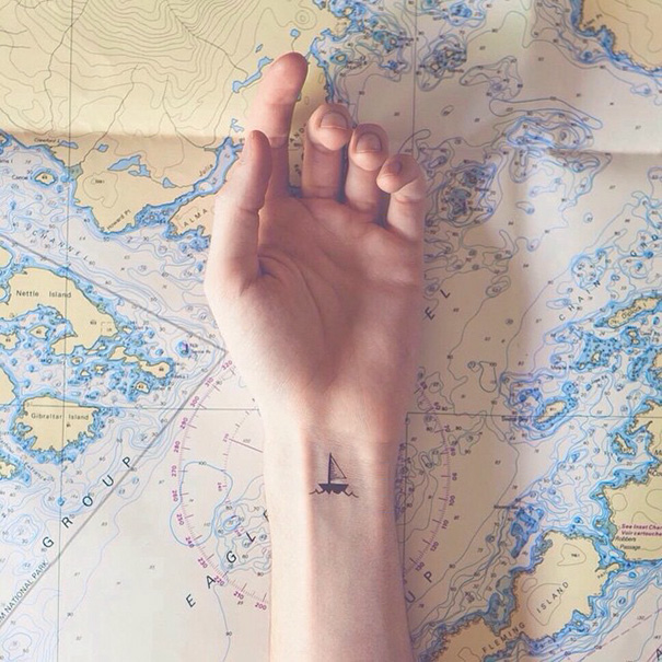 Minimalist tattoo of a sailboat on a wrist, set against a nautical map background.