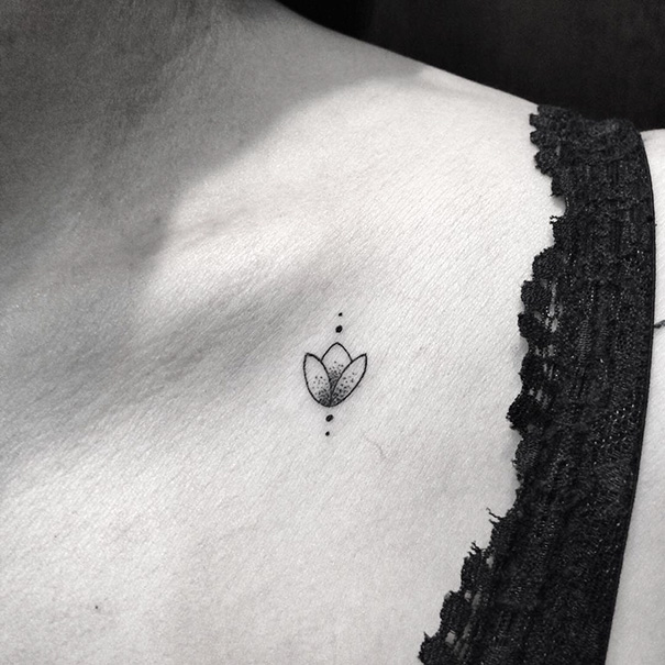Minimalist tattoo of a small flower inked on the collarbone, adjacent to black lace fabric.