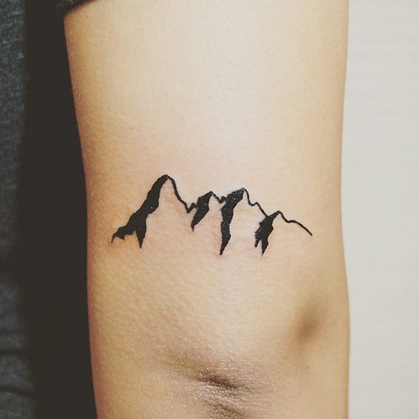 Minimalist tattoo of a mountain range on an arm.