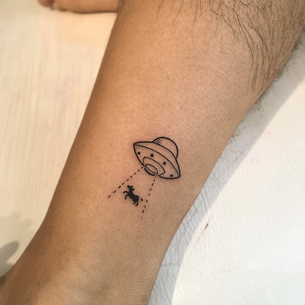 Minimalist tattoo of a UFO abducting a cow on an ankle.