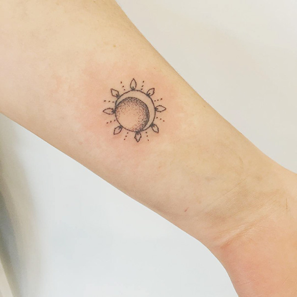 Minimalist tattoo of a sun and crescent moon on the forearm.