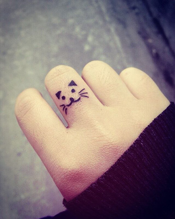 Minimalist cat face tattoo on finger, showcasing simple and stylish ink design.
