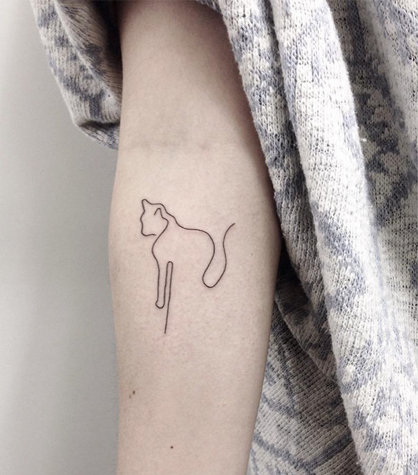 Minimalist tattoo of a simple cat line design on an arm.