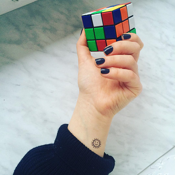 Hand holding a Rubik's Cube, with a minimalist sun tattoo on the wrist.