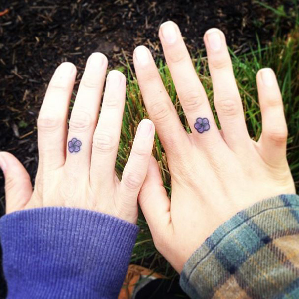 Two hands displaying small minimalist flower tattoos on their fingers.