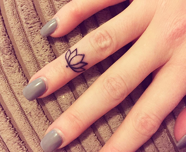 Minimalist tattoo of a lotus outline on a finger with gray nail polish.