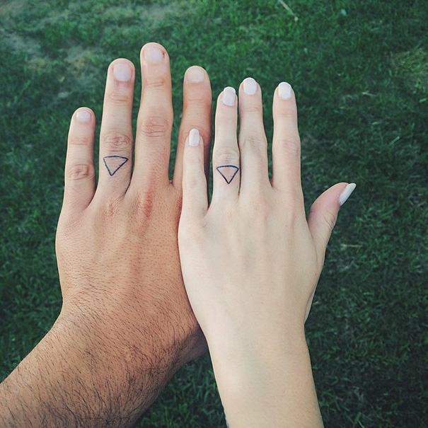 Minimalist tattoos of triangles on two hands, one male and one female, on a grass background.