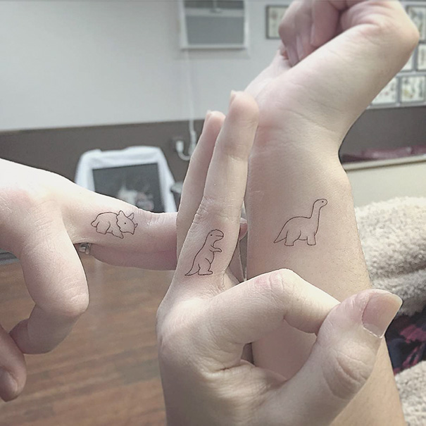 Minimalist dinosaur tattoos on wrists and fingers, featuring simple outlines and clean designs.