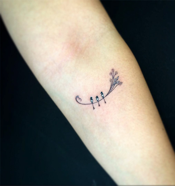 Minimalist tattoo of three birds on a branch with delicate details on forearm.