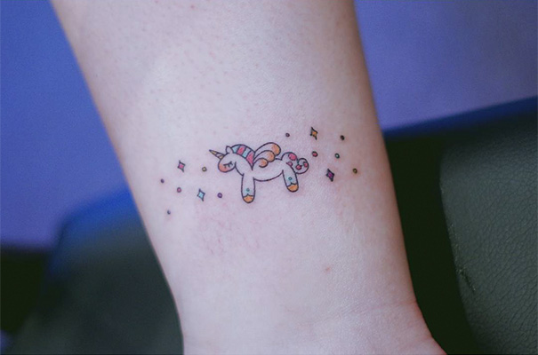 Minimalist unicorn tattoo with colorful details on forearm.
