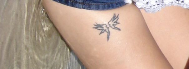 Minimalist tattoo of a small bird design on a woman's thigh.