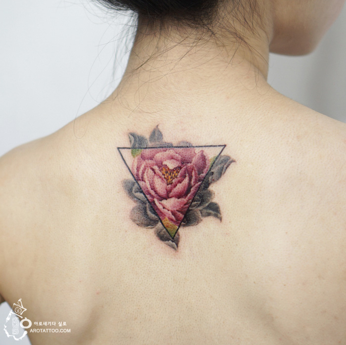 Watercolor-style flower tattoo on a person's upper back, featuring a pink rose within a triangle outline. Watercolor-style flower tattoo on a person's upper back, featuring a pink rose within a triangle outline.