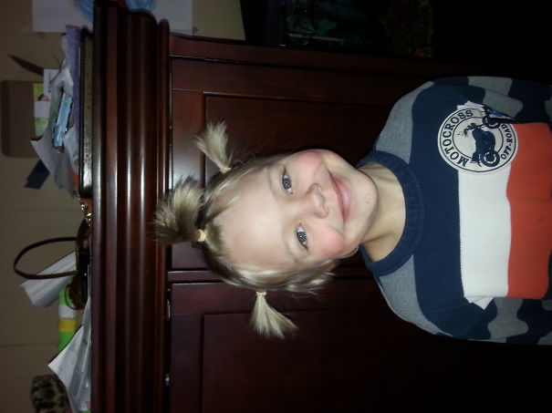 Child with crazy hair styled in spiky pigtails, smiling in a striped sweater.