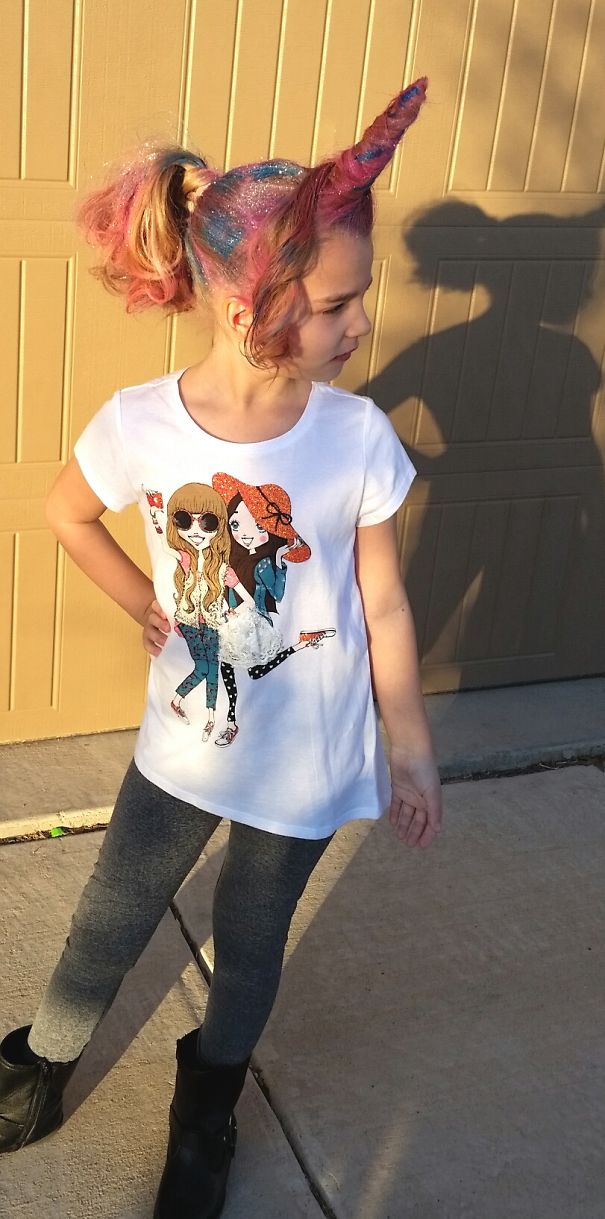 Child with a colorful unicorn hairstyle for a crazy hair day, wearing a graphic T-shirt, posing confidently outdoors.