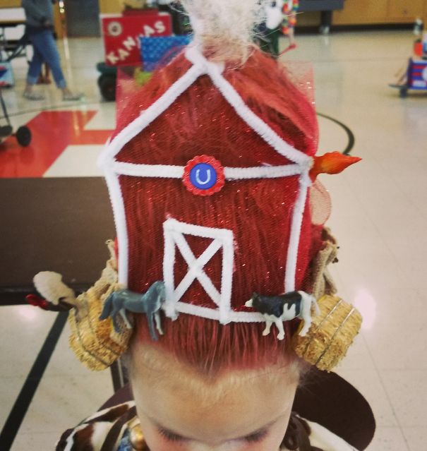 Child with a red barn-themed hairstyle, featuring farm animals and hay, for Crazy Hair Day.