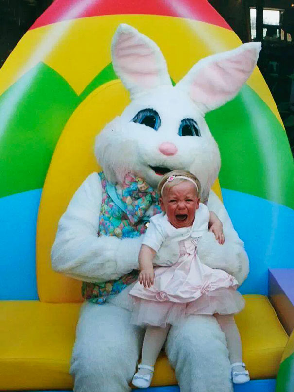 Vintage Easter Bunny costume with a crying child on its lap in front of a colorful background.