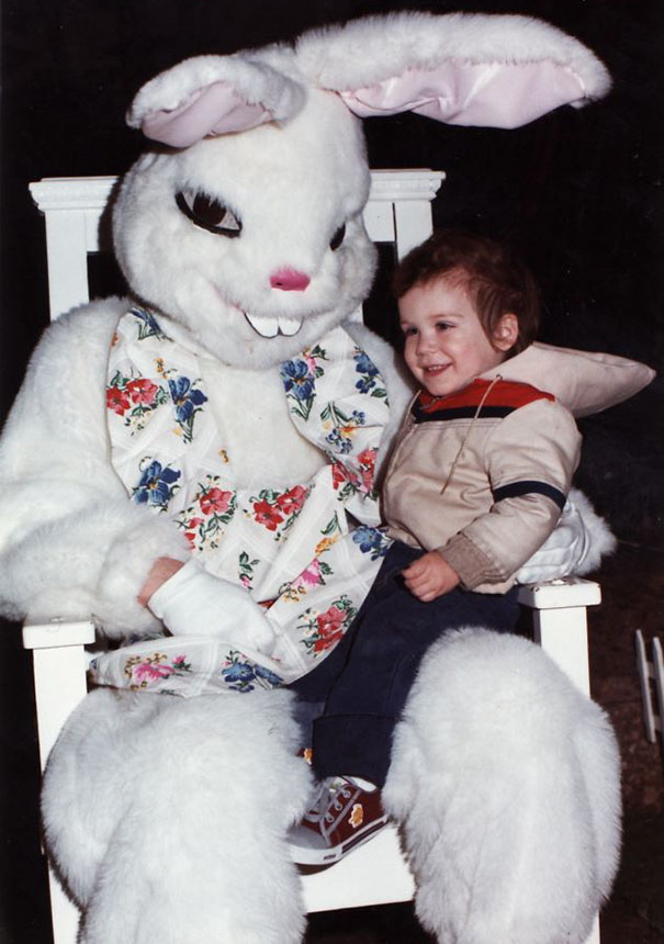 A child sitting on the lap of a vintage Easter bunny with a floral vest, showcasing a mix of joy and eeriness.