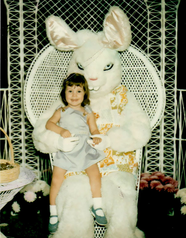 Child sitting on a vintage Easter Bunny's lap, with unsettling bunny expression, surrounded by floral decor.