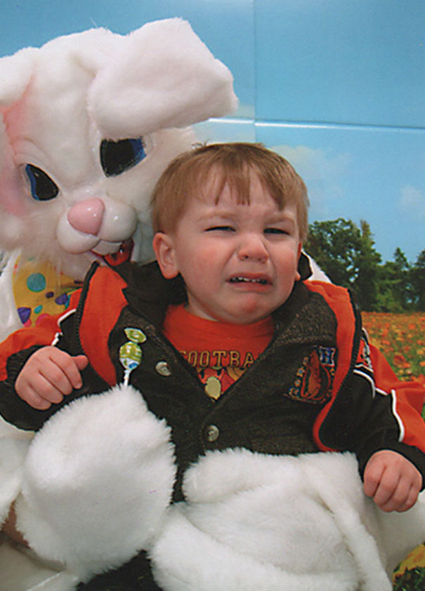 A child appears frightened sitting on a vintage Easter Bunny's lap, wearing an orange and brown jacket.