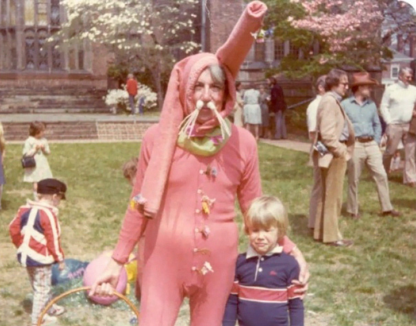 Vintage Easter Bunny costume with a pink outfit and child, creating a surreal, unsettling scene on a grassy outdoor setting.